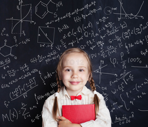 Kids mathematics education concept. Happy little girl math student on school blackboard background with hand drawings science formula pattern