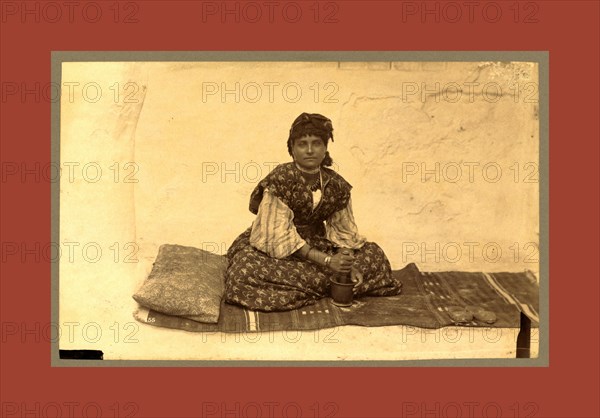 woman, full-length portrait, seated on rug on ground, facing front, using mortar and pestle, Constantine, Algeria, Neurdein brothers 1860 1890, the Neurdein photographs of Algeria including Byzantine and Roman ruins in Tébessa and Thamugadi; mosques, shrines, public buildings, palaces, and street scenes in Mostaganem, Biskra, Algiers, Tlemcen, Constantine, Oran, and Sidi Bel AbbÃ¨s; and the cathedral at Carthage. Portraits of Algerian people include Berbers, Ouled NaÃ¯l women, and prisoners in Annaba. Tunisian views include mosques, buildings, and street scenes in Tunis.