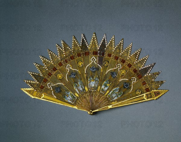 Brise Fan:  Gothic Revival Style, c. 1830. England (probably), 19th century. Gilt metal, enamel, horn, pigment, spangles, ribbon; radius: 18.8 cm (7 3/8 in.); spread: 35 cm (13 3/4 in.).