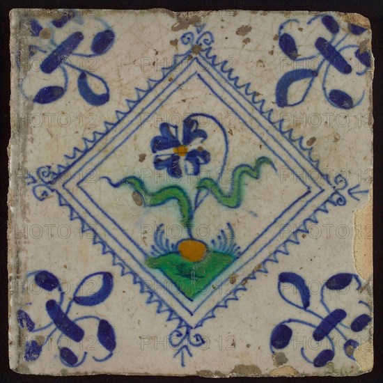 Tile, flower on ground in orange, green and blue on white, inside serrated square, corner pattern french lily, wall tile