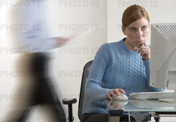 Woman at computer with person passing.