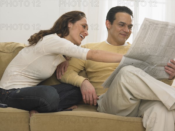 Couple relaxing reading newspaper together.