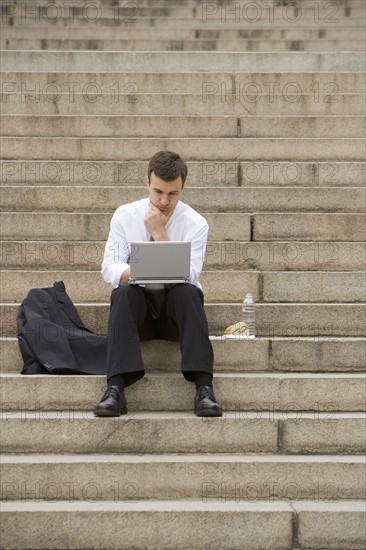 Man sitting outdoors on stairs with laptop.