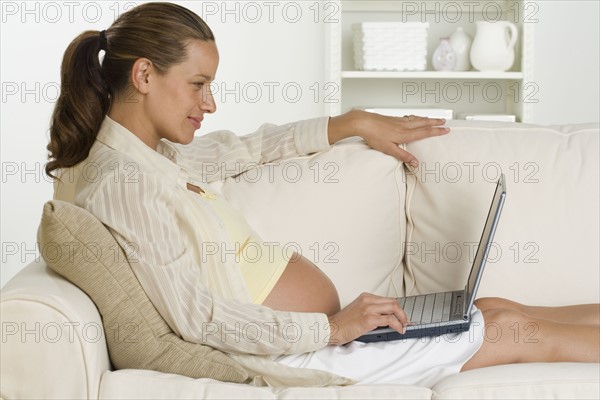 Pregnant woman on sofa using laptop.