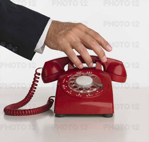 Close up studio shot of man reaching for rotary telephone.