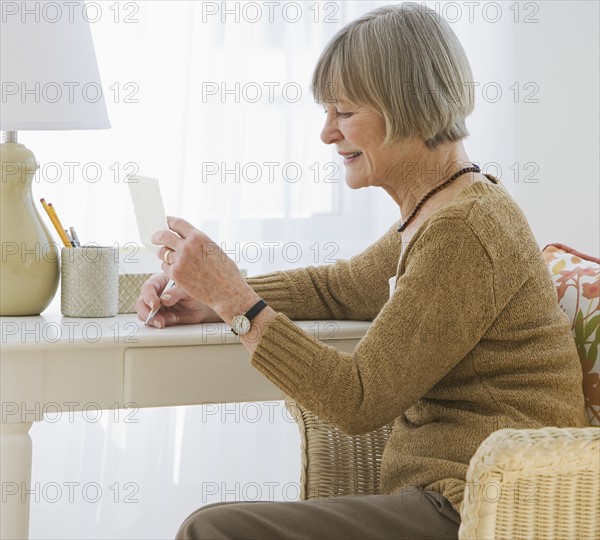 Senior woman reading letter at desk.