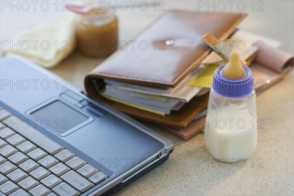 Laptop, planner and baby bottle on table.