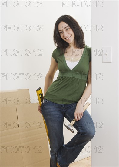 Woman leaning on wall with hammer and level indoors. Date : 2006