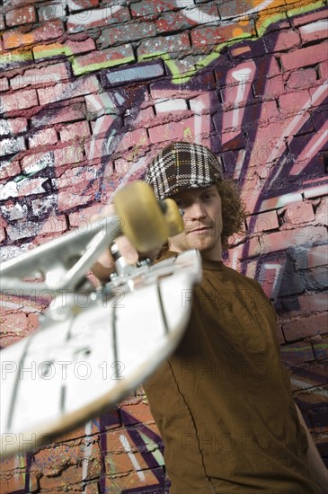 Young man with skateboard in front of graffitied wall. Date : 2007