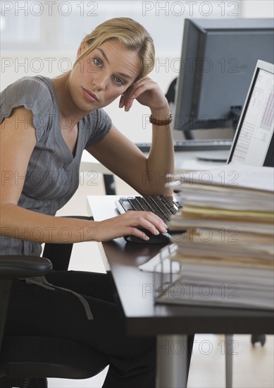 Businesswoman with stack of paperwork on desk.