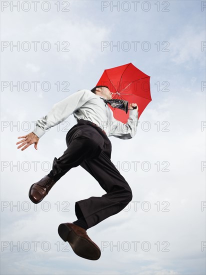 Businessman with umbrella jumping in mid-air. Date: 2008
