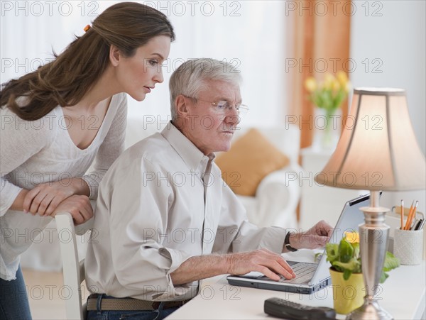 Daughter helping senior father with computer.