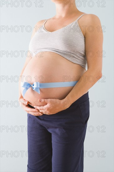 Pregnant woman’s belly wrapped in blue ribbon. Photographe : Jennifer L. Boggs