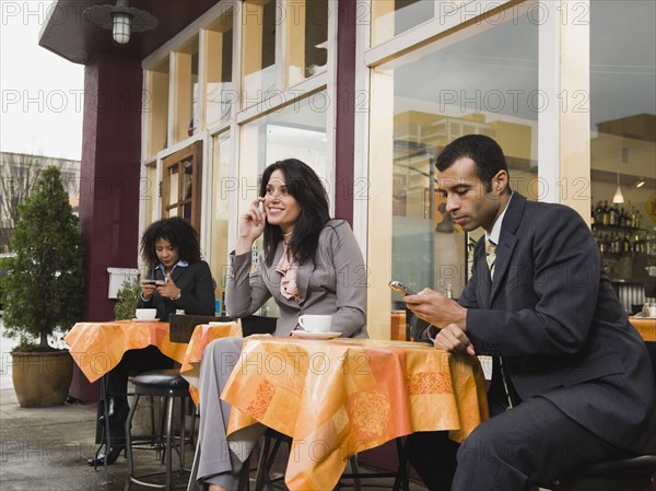 Businesspeople using cell phones at outdoor cafe.