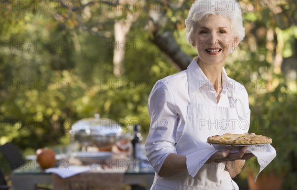 Senior woman standing in garden holding plate with pie. Photographe : mark edward atkinson