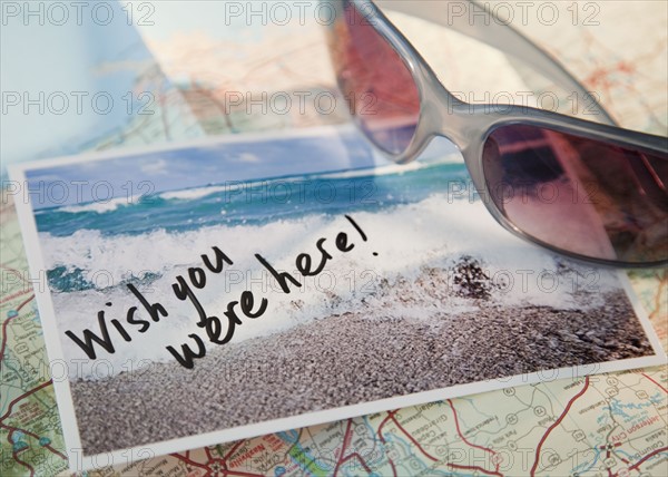 Close-up of sunglasses and postcard on map. Photographe : Jamie Grill