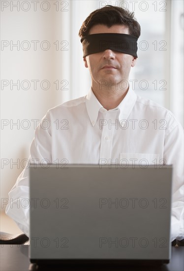 Businessman using laptop while blindfolded.