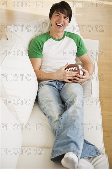 Male football fan relaxing on couch. Photographe : Daniel Grill
