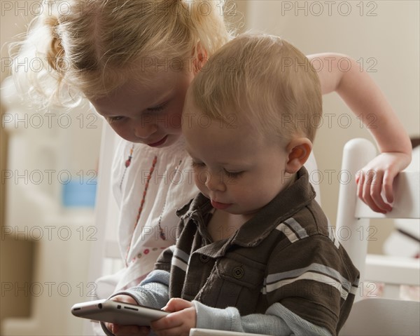 Young siblings looking at cell phone together. Photo : Mike Kemp