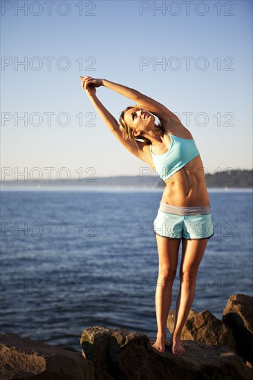 Athletic woman stretching by the ocean. Photo : Take A Pix Media