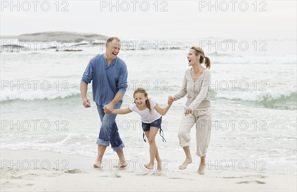 Girl (10-11) playing on beach with parents. Photo : Momentimages