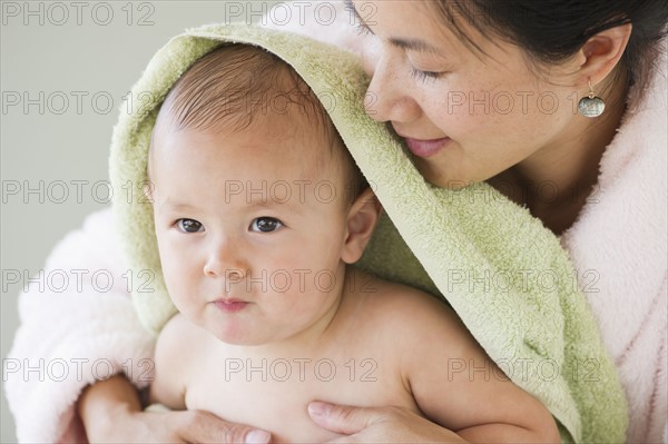 Mother holding baby boy (12-17 months) wrapped in towel. Photo : Daniel Grill
