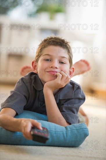 Boy (10-11) smiling and holding remote control. Photo : Daniel Grill