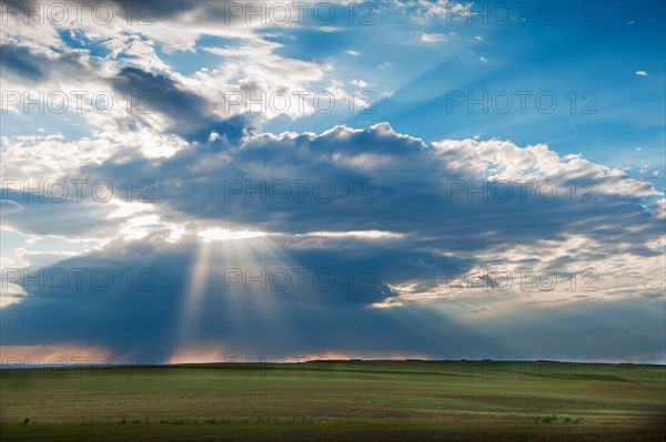 Sunrays shining through clouds over field.