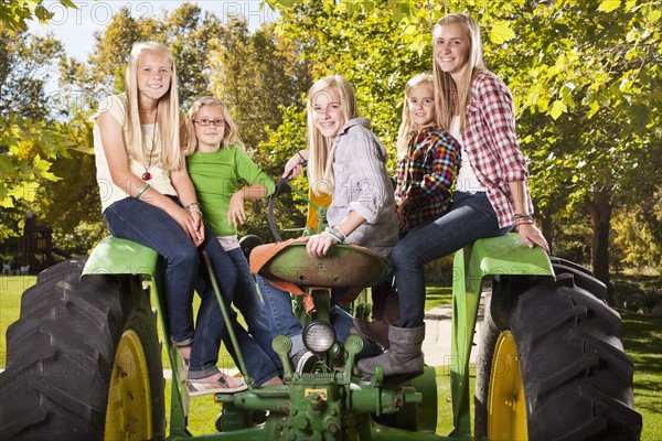 USA, Utah, family portrait of sisters (6-7, 8-9, 12-13, 14-15, 16-17) sitting on tractor. Photo : Tim Pannell