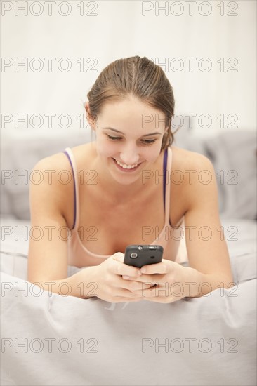 Young woman using mobile phone on bed. Photo : Mike Kemp