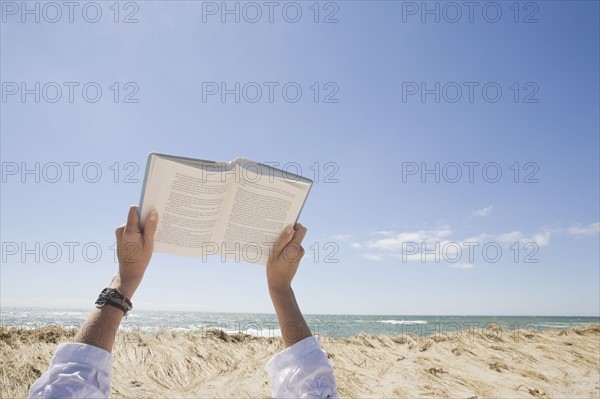 USA, Massachusetts, woman's hands on beach holding book. Photo : Chris Hackett