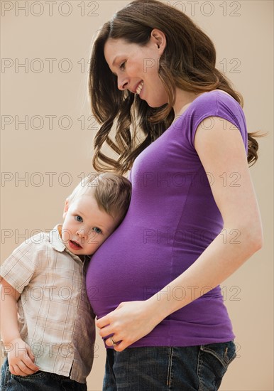 Portrait of boy (2-3) leaning pregnant mother's belly. Photo : Mike Kemp