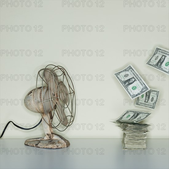 Electric fan blowing on heap of dollar banknotes.