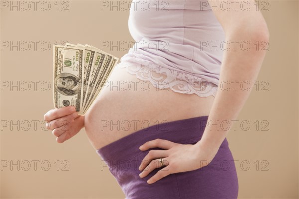 Young pregnant woman holding money roll of Dollars. Photo: Mike Kemp