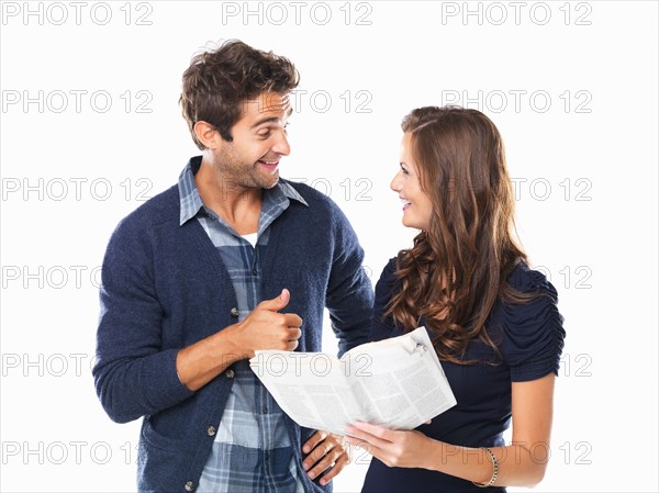 Studio shot of young couple with newspaper smiling and looking at each other. Photo: momentimages