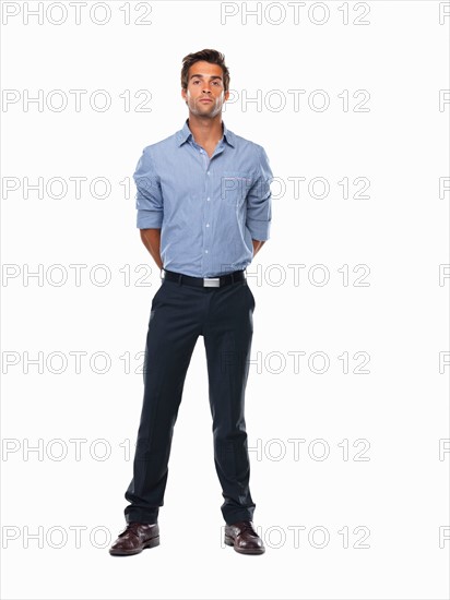 Studio shot of young business man standing with hands behind back. Photo : momentimages