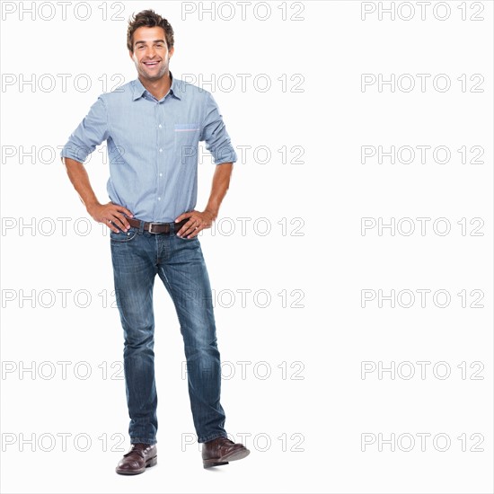 Studio shot of young man standing with hands on hips and smiling. Photo: momentimages