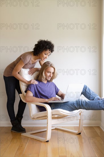 Young woman looking at man using laptop at home. Photo: Rob Lewine