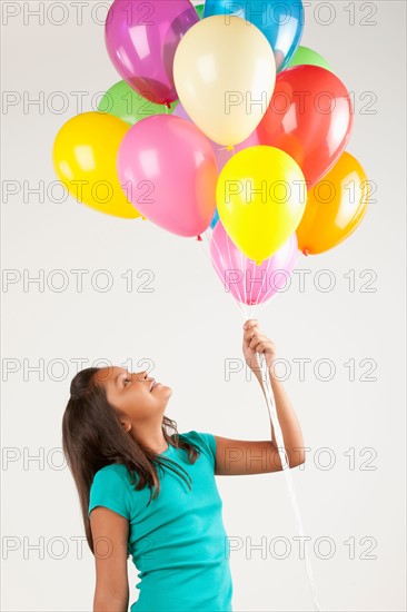 Portrait of smiling girl (10-11) holding balloons, studio shot. Photo: Rob Lewine