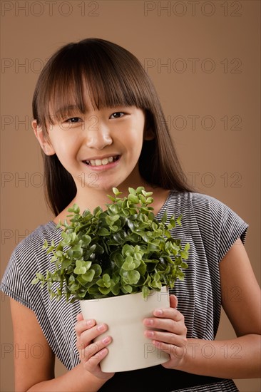 Studio portrait of girl (10-11) holding potted plant. Photo: Rob Lewine