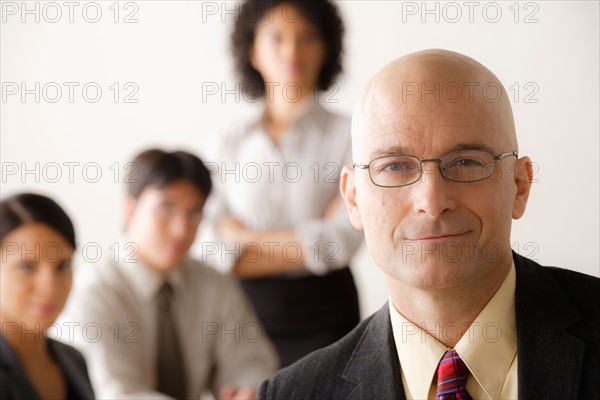 Mature businessman looking at camera, business team in background. Photo: Rob Lewine