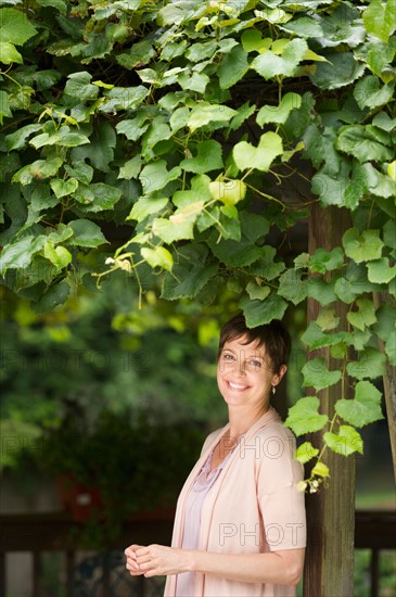Portrait Of Mature Woman Leaning Against Wooden Post Overgrown With Ivy
