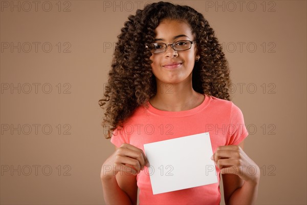 Studio portrait of girl (10-11) holding blank sheet of paper. Photo : Rob Lewine