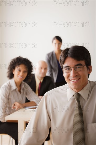Smiling businessman looking at camera, business team in background. Photo: Rob Lewine