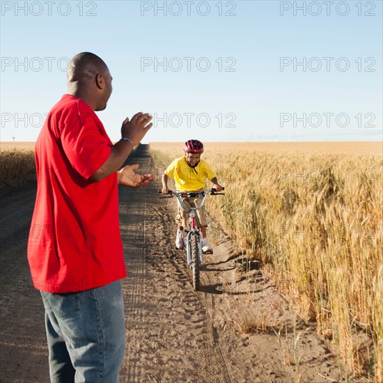 Father clapping as son (8-9) is cycling along dirt road in fields. Photo: Erik Isakson