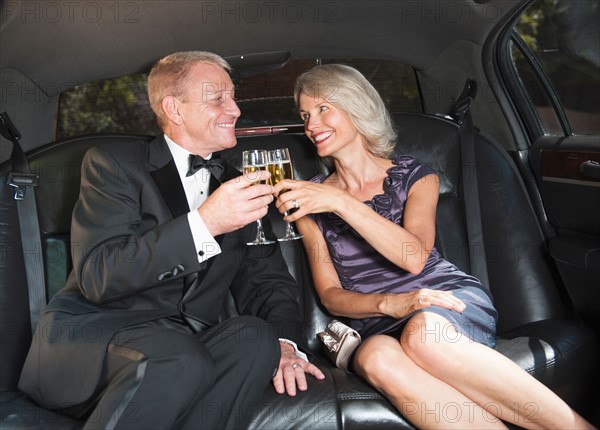 Parents of bride drinking champagne inside limousine.