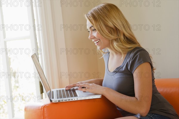 Young woman sitting on sofa using laptop. Photo : Rob Lewine
