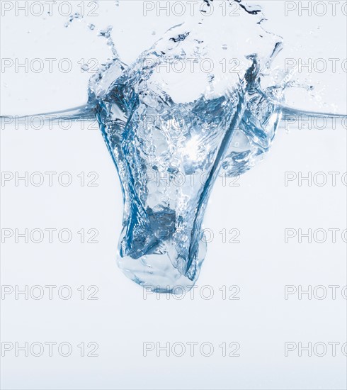 Ice cube splashing into water, studio shot. Photo: Daniel Grill
