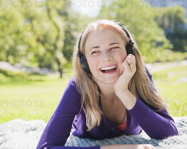 USA, New York, New York City, Manhattan, Central Park, Young woman lying on grass and listening to music. Photo : Daniel Grill