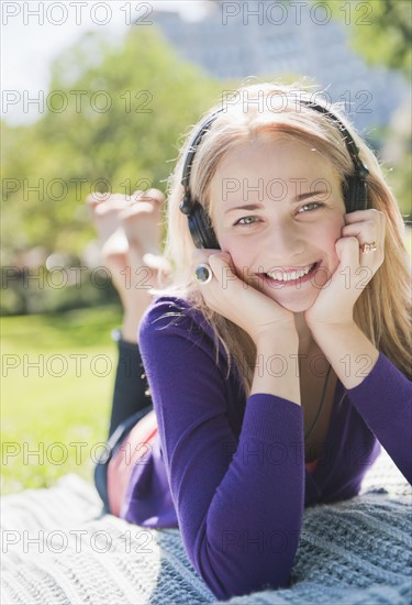 USA, New York, New York City, Manhattan, Central Park, Young woman lying on grass and listening to music. Photo : Daniel Grill
